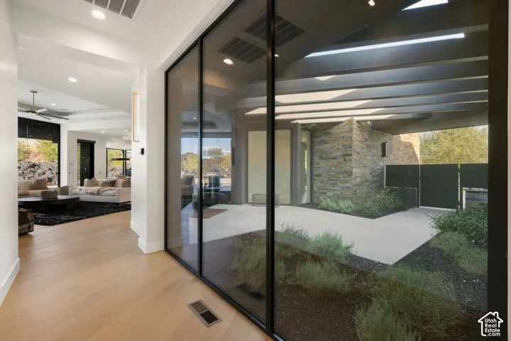 Floor-to-ceiling glass wall, light-toned wood-finish flooring, recessed ceiling lighting, stone exterior accent wall, and concrete patio