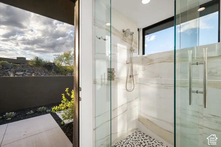 Walk-in shower featuring large-format wall tile with natural veining, a mosaic tile floor, chrome shower fixtures, and a glass door, with an exterior patio featuring concrete pavers and desert landscaping