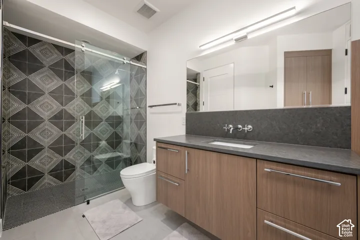 Bathroom featuring a floating wood-finish vanity, solid-surface countertop, wall-mounted faucet, walk-in glass-enclosed shower with geometric tile surround, and an integrated full-width mirror