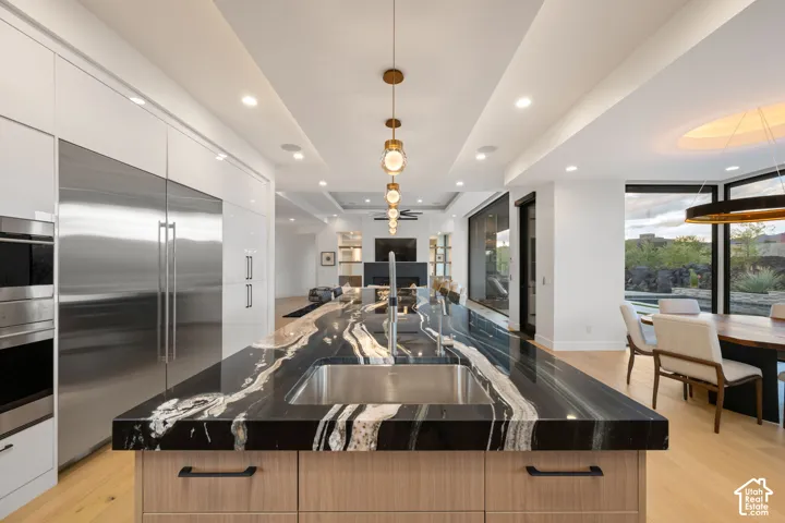 Kitchen featuring a large center island with a high-contrast natural stone countertop, integrated stainless steel appliances, recessed ceiling lighting, and wood-finish flooring
