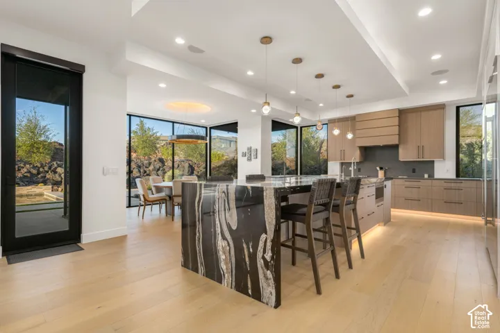 Kitchen featuring a waterfall-edge island with stone detailing, custom wood-finish cabinetry, recessed lighting, drop pendant fixtures, and floor-to-ceiling windows