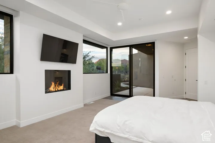 Recessed fireplace with stone surround, large-format sliding glass door, high ceilings with recessed lighting, and wall-to-wall carpeting