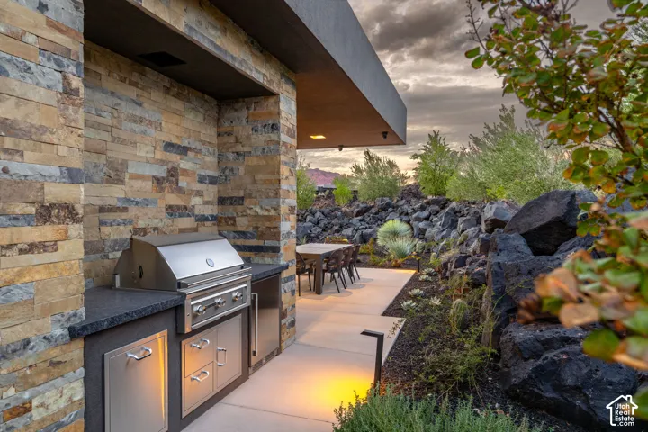 Outdoor kitchen featuring a stone-clad backsplash, stainless steel built-in grill, stone-finish countertop, stainless steel storage cabinetry, and concrete patio flooring