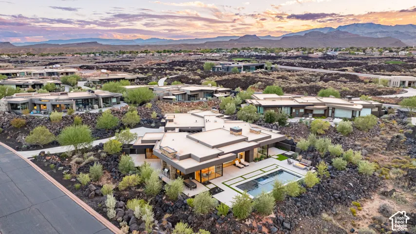 Modern single-story residence featuring a flat roofline, integrated swimming pool, paved patio, natural stone landscaping, and mountainous backdrop