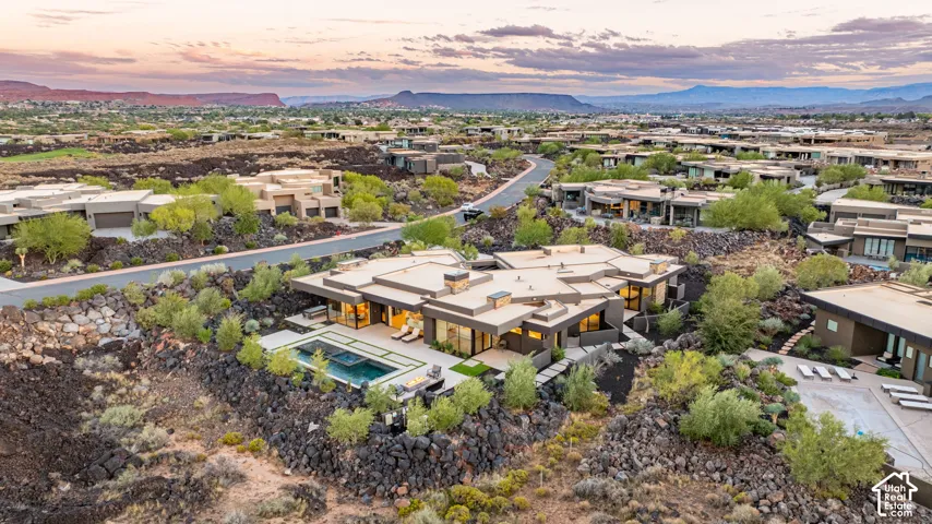 Contemporary residence featuring a low-profile flat roofline, integrated swimming pool with spa, expansive patio hardscaping, and prominent volcanic rock landscaping