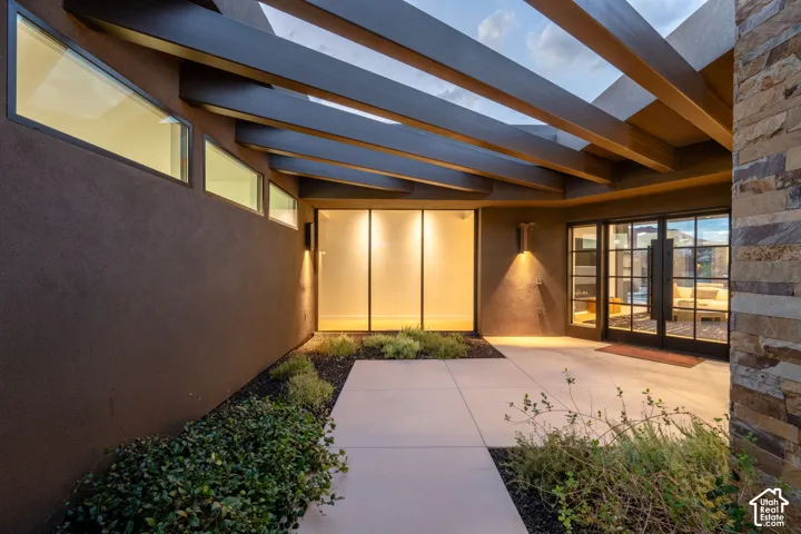Covered entrance featuring a timber pergola, stacked stone facade, concrete patio, clerestory windows, and glass-paneled double doors