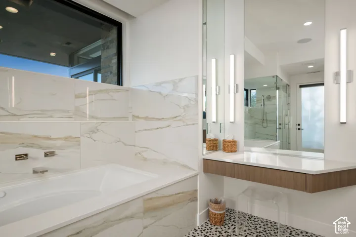 Soaking tub featuring large-format tile surround, wall-mounted polished chrome faucet, floating wood-finish vanity, integrated countertop, and dual linear light fixtures