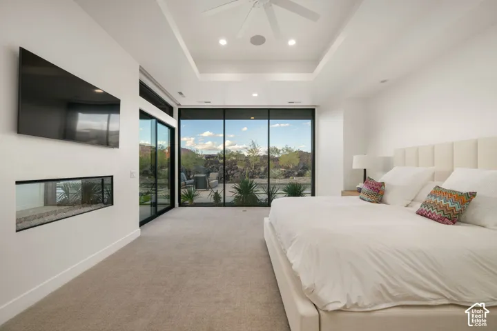 Floor-to-ceiling glass walls, recessed tray ceiling, built-in horizontal fireplace, neutral carpeting, and integrated ceiling lighting