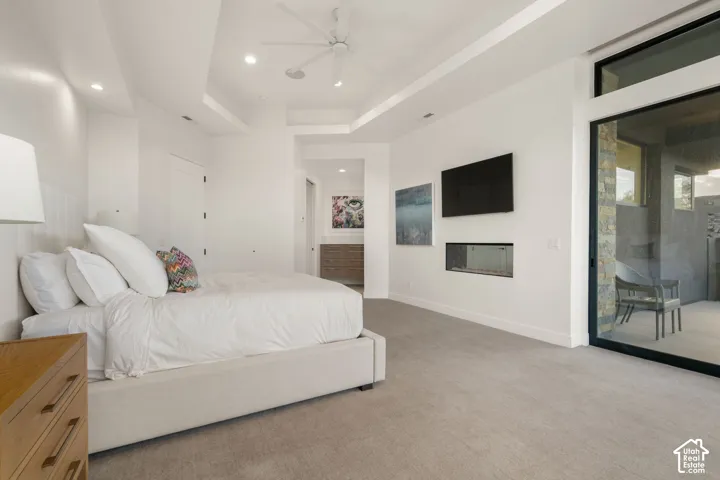 Tray ceiling with recessed lighting, built-in horizontal fireplace, floor-to-ceiling glass sliding door, and neutral wall-to-wall carpeting