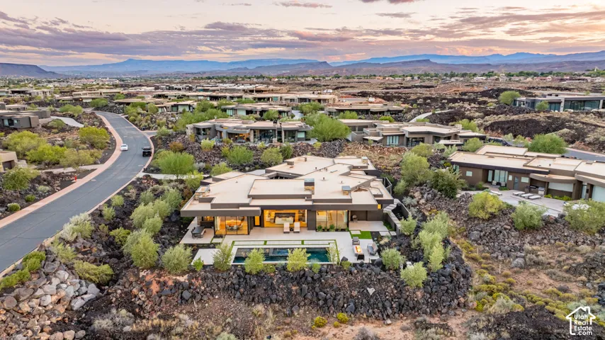 Contemporary architectural residence featuring a flat roofline, floor-to-ceiling glass windows, a private swimming pool, and stone hardscaping, situated amidst volcanic rock terrain with mountain backdrop