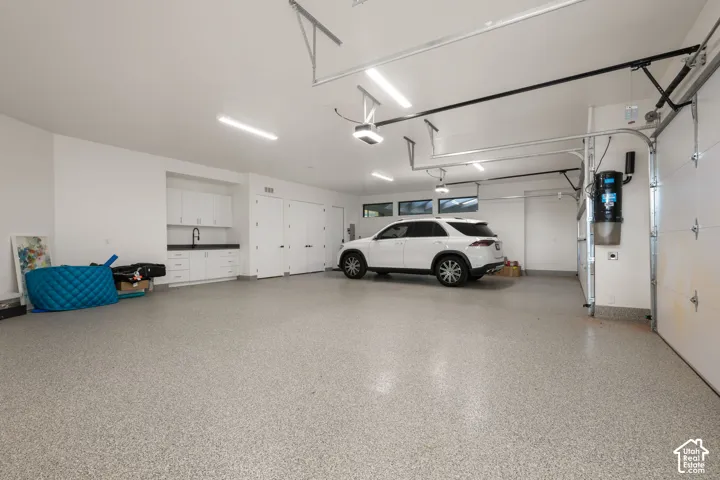 Finished garage featuring epoxy flooring, built-in cabinetry with a dark countertop and utility sink, overhead LED lighting, and horizontal transom windows