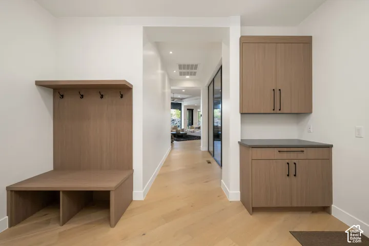 Built-in wood-finish cabinetry featuring open storage, integrated coat hooks, and matching lower and upper storage units with matte black hardware and dark solid-surface countertops, set against wood-finish flooring