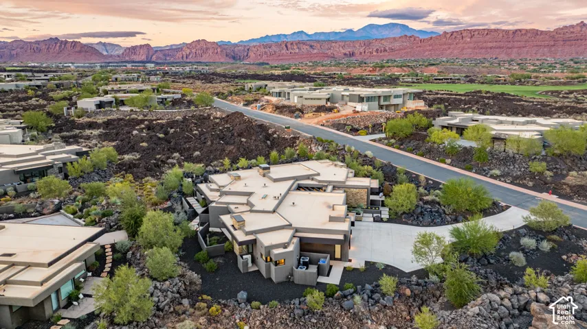 Modern single-story residence featuring a flat roofline, concrete driveway, stone facade accents, and desert landscaping set against a backdrop of red rock mountain formations