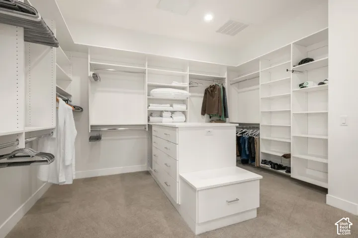 Walk-in closet featuring floor-to-ceiling white built-in shelving, integrated hanging rods, a central island with soft-close storage drawers, and wall-to-wall carpeting
