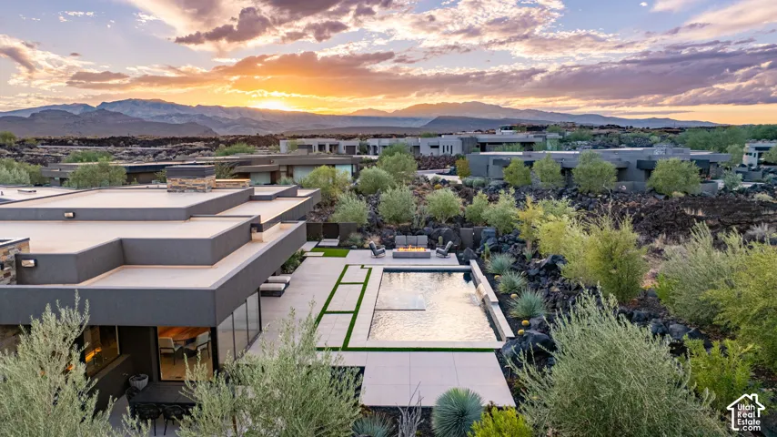 Contemporary exterior featuring flat roof lines, rectangular in-ground swimming pool, stone-tiled patio, integrated fire feature, and mountain backdrop