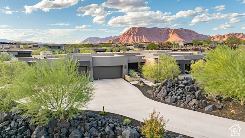 Modern desert architecture featuring clean lines, a multi-car garage, stone masonry accents, a paved driveway, and dramatic mountain scenery