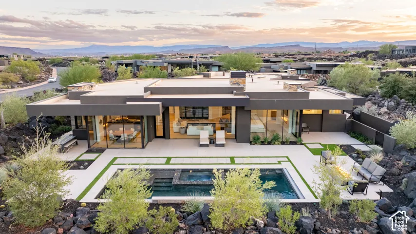 Modern single-level residence featuring expansive floor-to-ceiling glass walls, flat roof architecture, a custom swimming pool with integrated spa, and concrete patio hardscaping