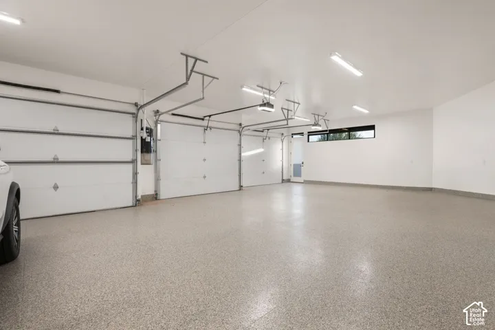 Three-car garage featuring epoxy-coated flooring, white interior walls, overhead LED lighting, and a single pedestrian door