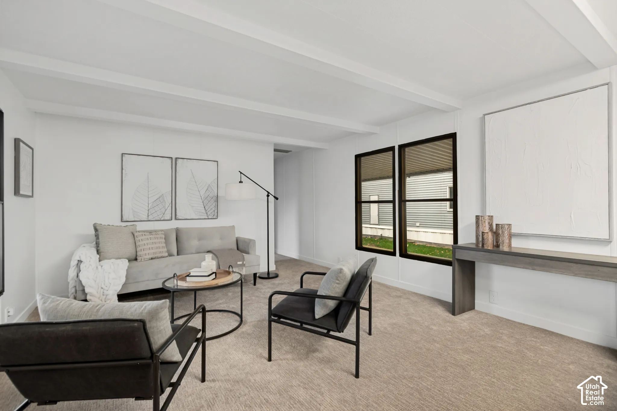 Living area featuring neutral carpeting, white walls, dark-framed dual-pane windows, and a ceiling accented with structural beams