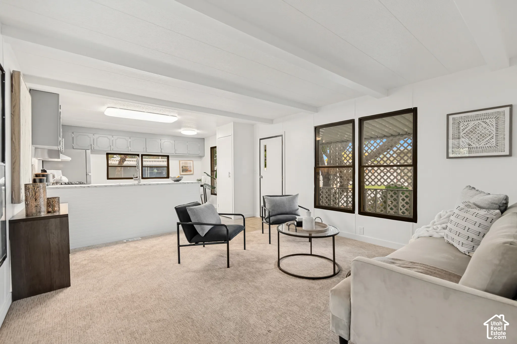 Open-concept interior featuring exposed beam ceilings, wall-to-wall carpeting, and a kitchen peninsula with stone-finish countertops
