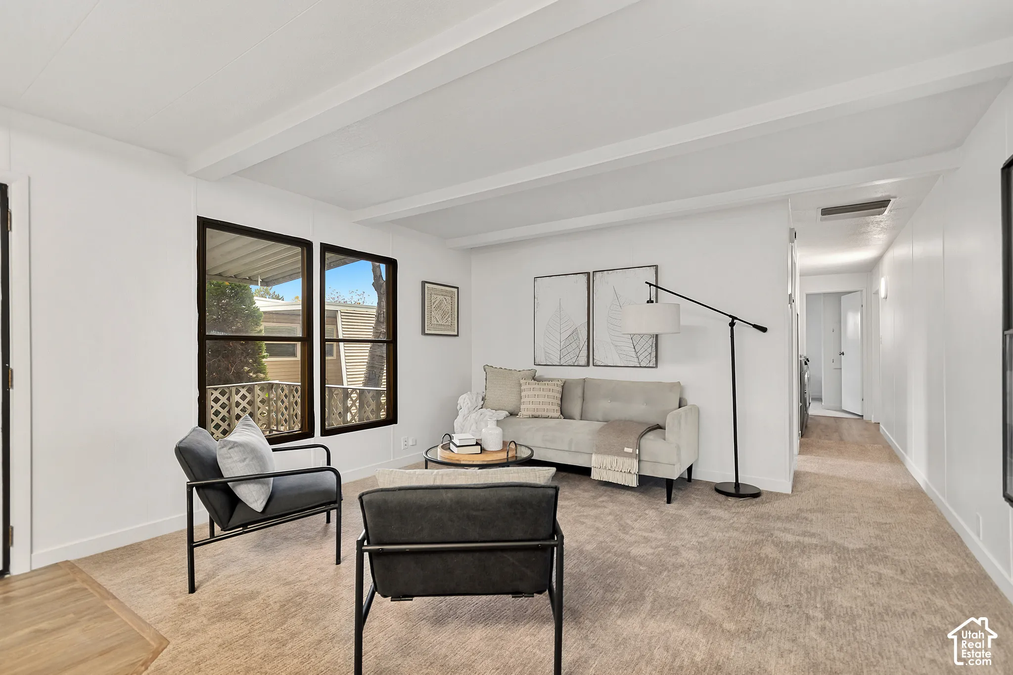 Living area featuring exposed ceiling beams, neutral carpeting, and large windows with dark-finish frames