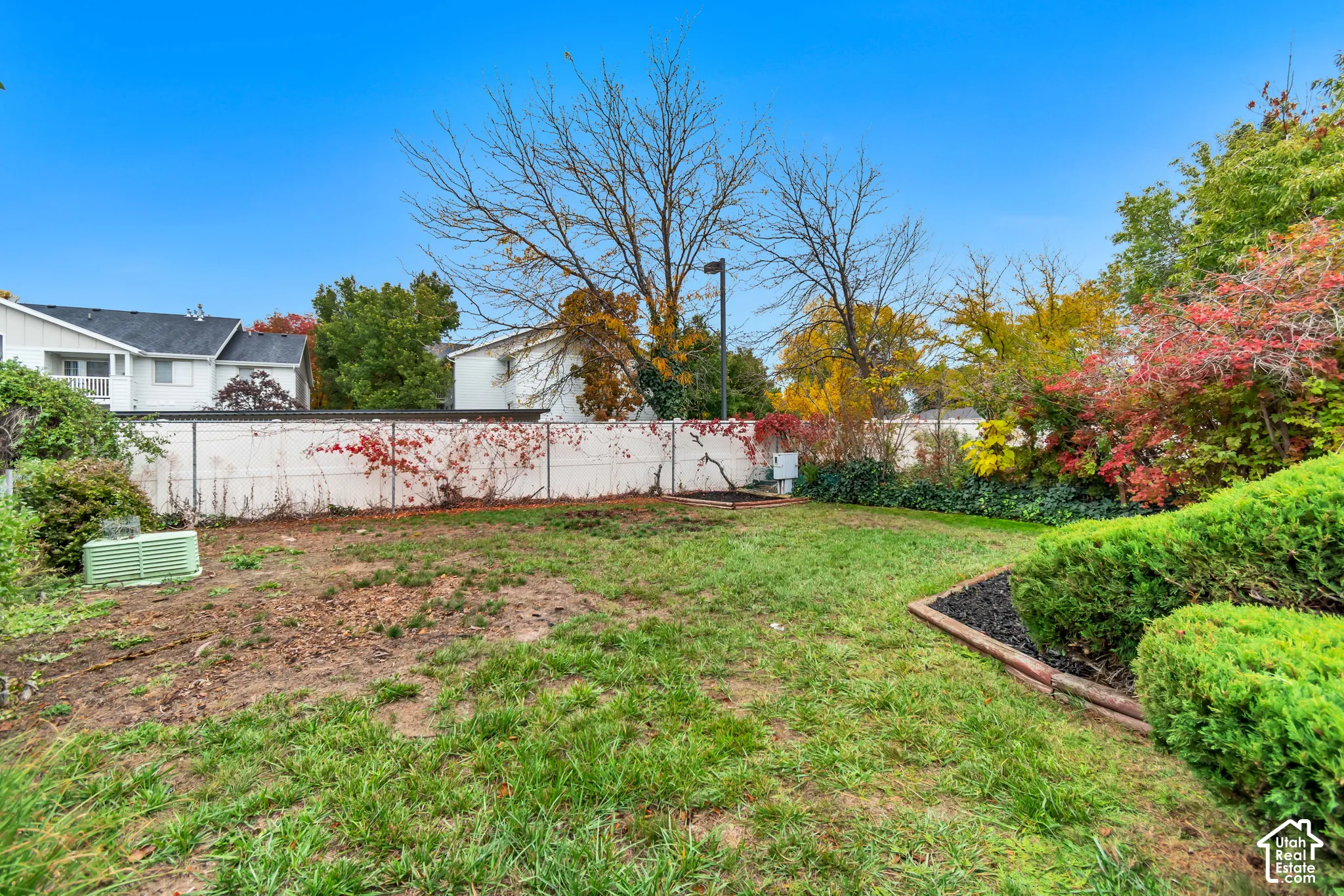 Rear yard featuring a grass lawn, perimeter vinyl fencing, and established perimeter shrubbery with a masonry border
