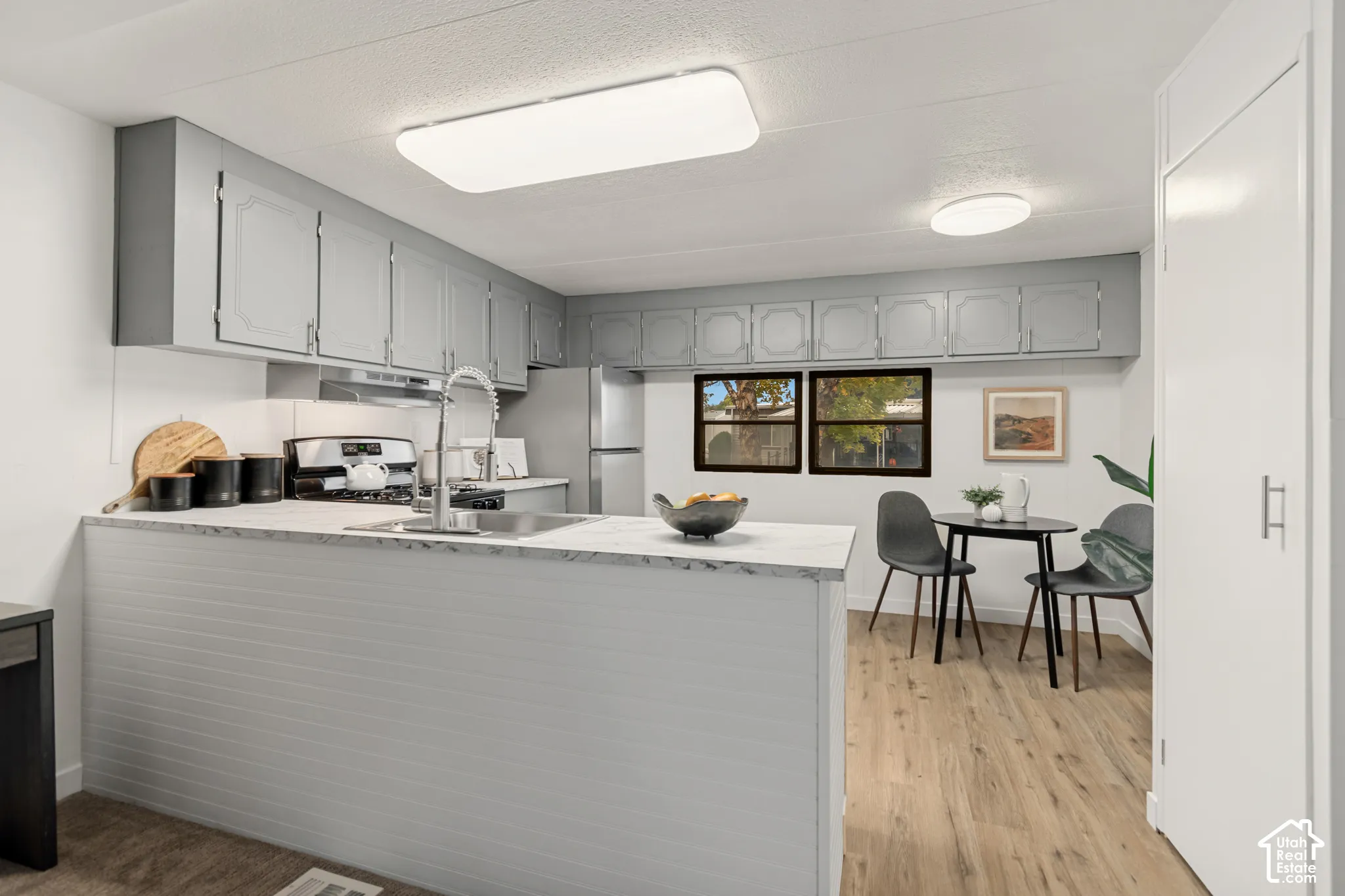 Kitchen featuring light gray cabinetry, solid surface countertop with peninsula seating, stainless steel sink with high-arc faucet, and wood-finish flooring