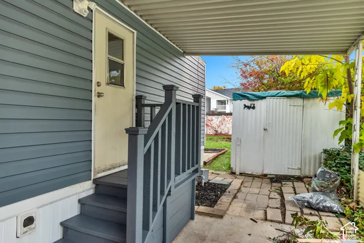Exterior entry featuring horizontal vinyl siding, a covered patio area, wooden stairs with matching railing, and an exterior storage structure