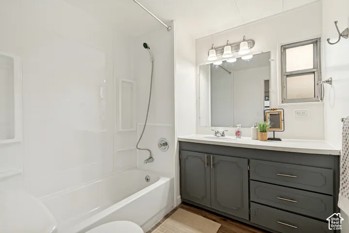 Bathroom featuring a vanity with dark-tone cabinetry, a wide vanity mirror, a three-bulb wall-mounted light fixture, and a tub-shower combination with a hand-held shower head