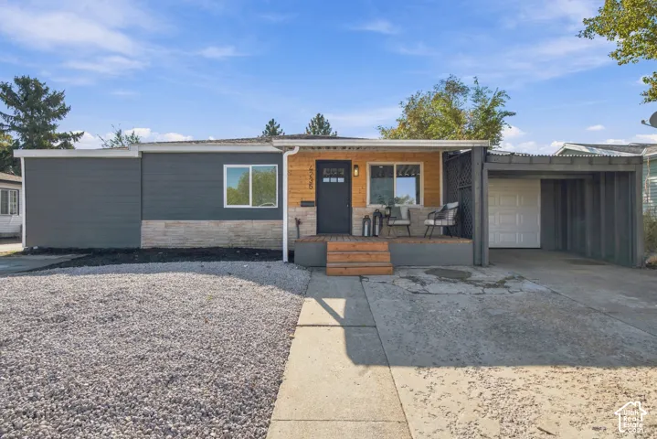 Single-story exterior featuring a mix of horizontal siding, stone veneer, and wood-panel accents, complemented by an attached carport and a raised wood-deck entrance