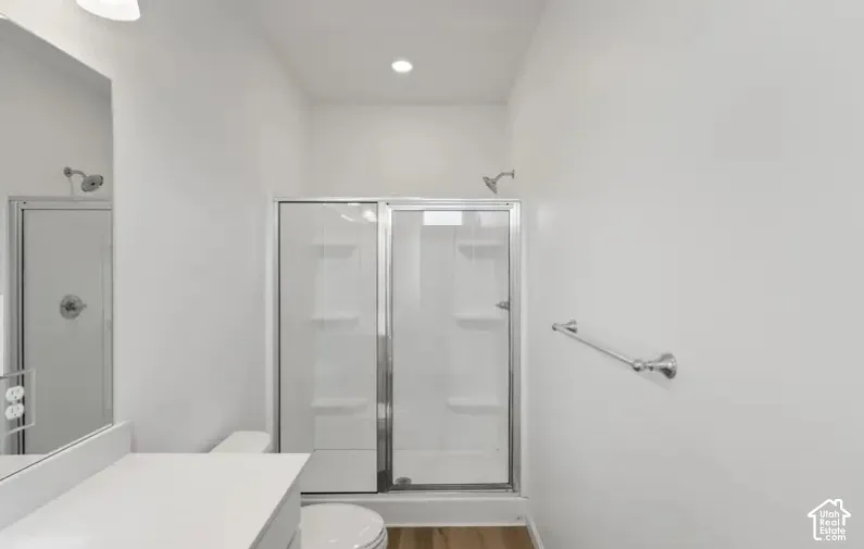 Bathroom featuring a shower stall with a glass door, built-in shelving, a wall-mounted metal towel bar, and wood-finish flooring