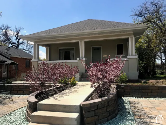 Craftsman-style residence featuring a covered front porch, concrete steps, tiered stone retaining walls, and paver hardscaping