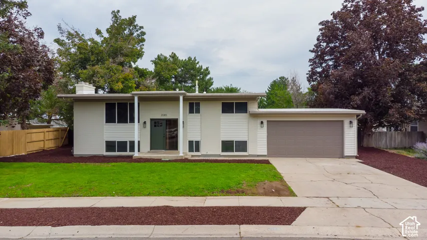 Split-level exterior featuring a two-tone siding facade, covered entryway, attached two-car garage, concrete driveway, and mature landscaping