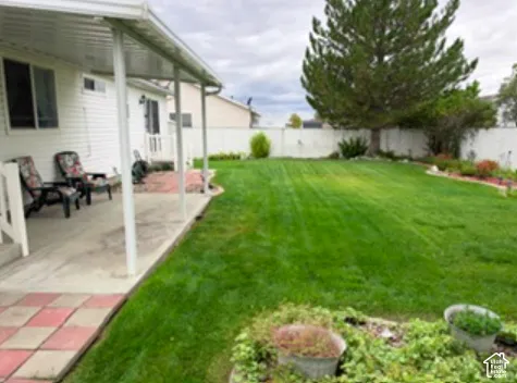Fenced backyard featuring a covered concrete patio, an expansive lawn, and mature evergreen trees