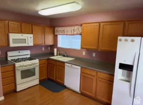 Kitchen featuring wood cabinetry, solid-surface countertops, dual-basin sink, and white appliances including a gas range and built-in microwave