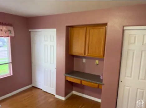 Built-in recessed desk with wood cabinetry and countertop, wood-finish flooring, and dual white paneled sliding closet doors