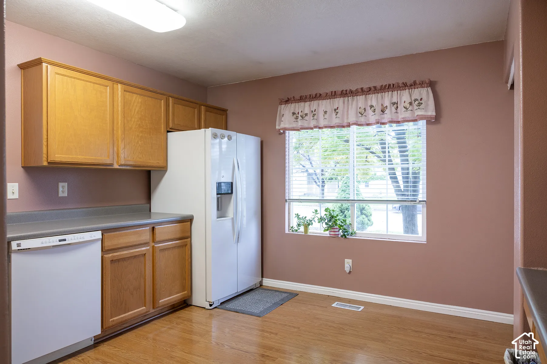 Kitchen area featuring wood-finish cabinetry, neutral solid-surface countertops, wood-finish flooring, and a window with exterior exposure