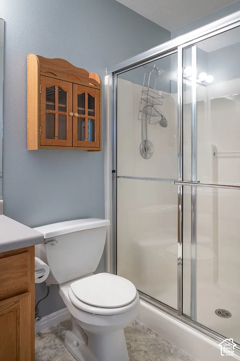 Bathroom featuring a shower stall with a glass enclosure, wood cabinetry, stone-finish countertop, and a wall-mounted wood cabinet with glass-panel doors