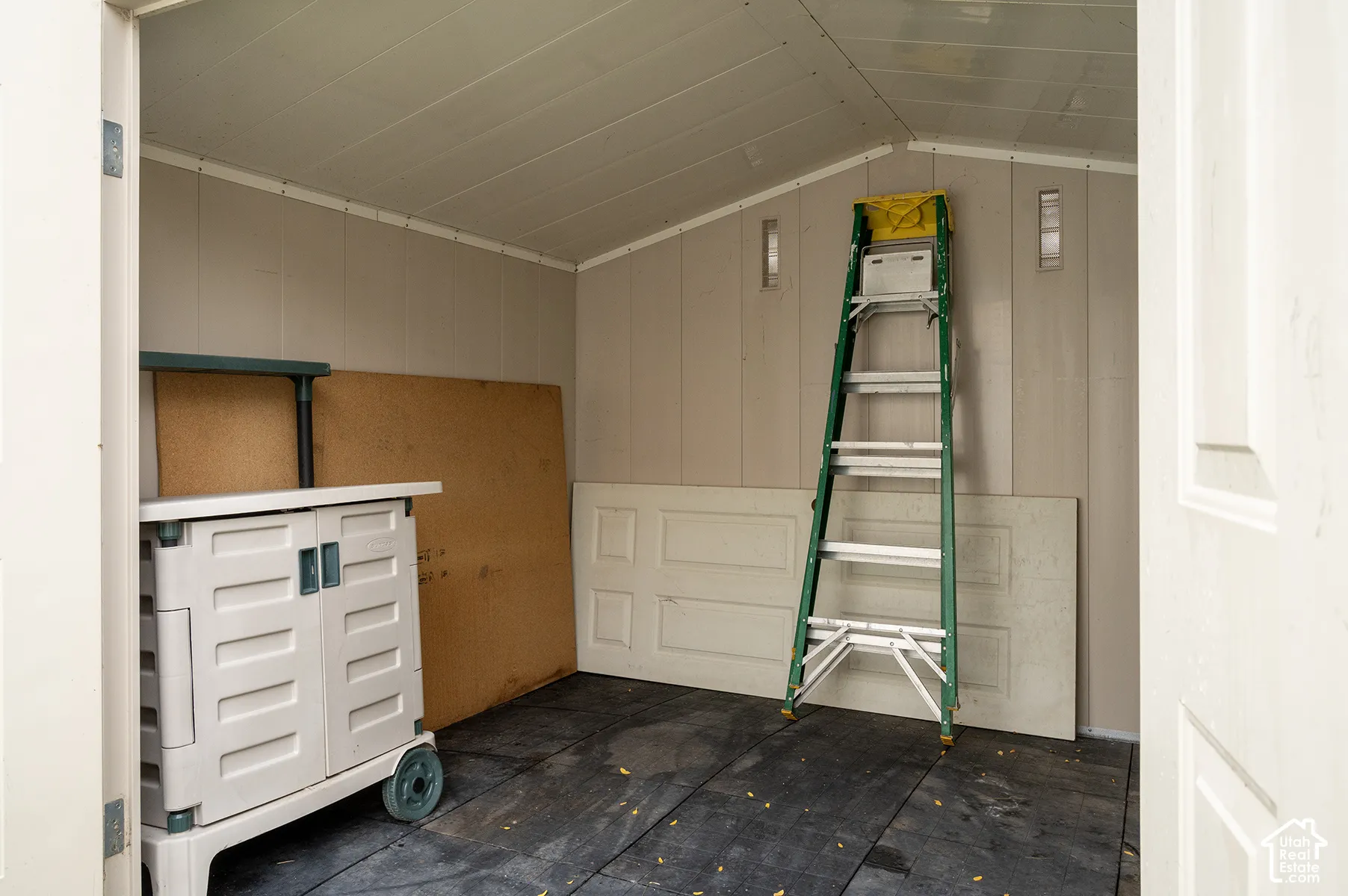 Enclosed storage structure featuring vertical wall panels, gable ceiling, and durable floor surfacing