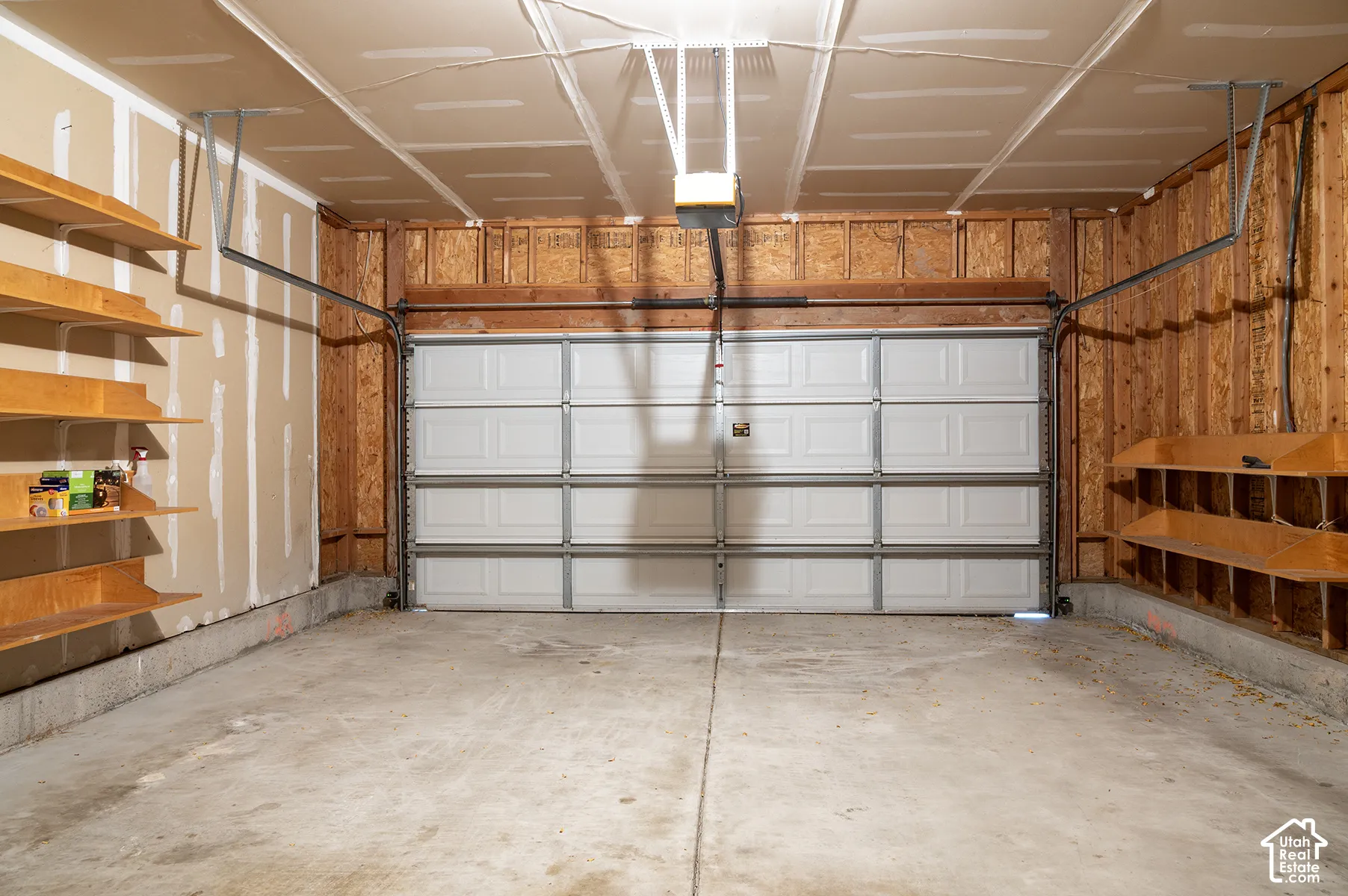 Multi-car garage featuring a sectional metal door, concrete flooring, built-in wooden shelving units, and an automated door opener