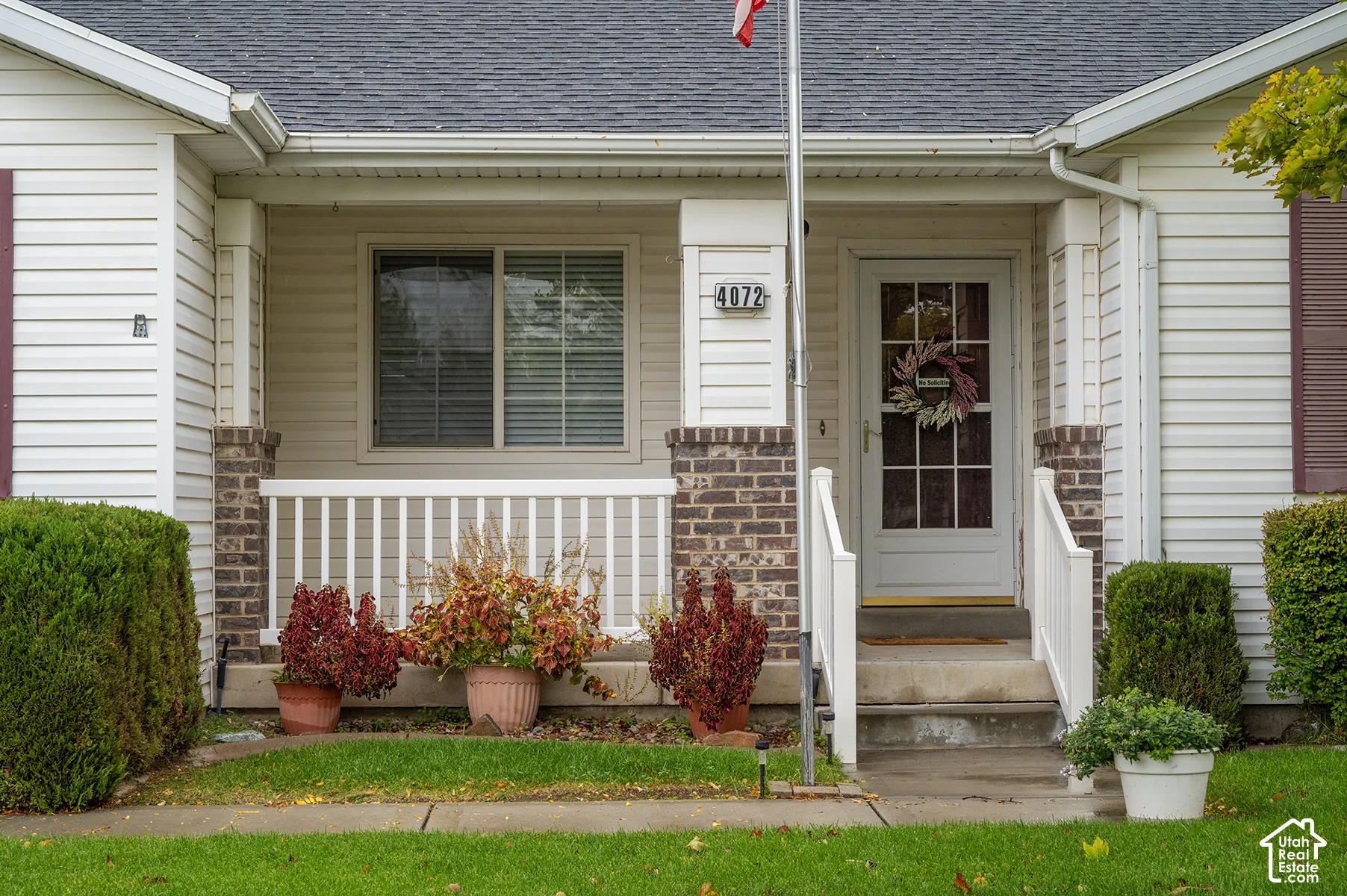 Covered front porch featuring white vinyl railings, brick-accented pillars, and a multi-pane glass entry door