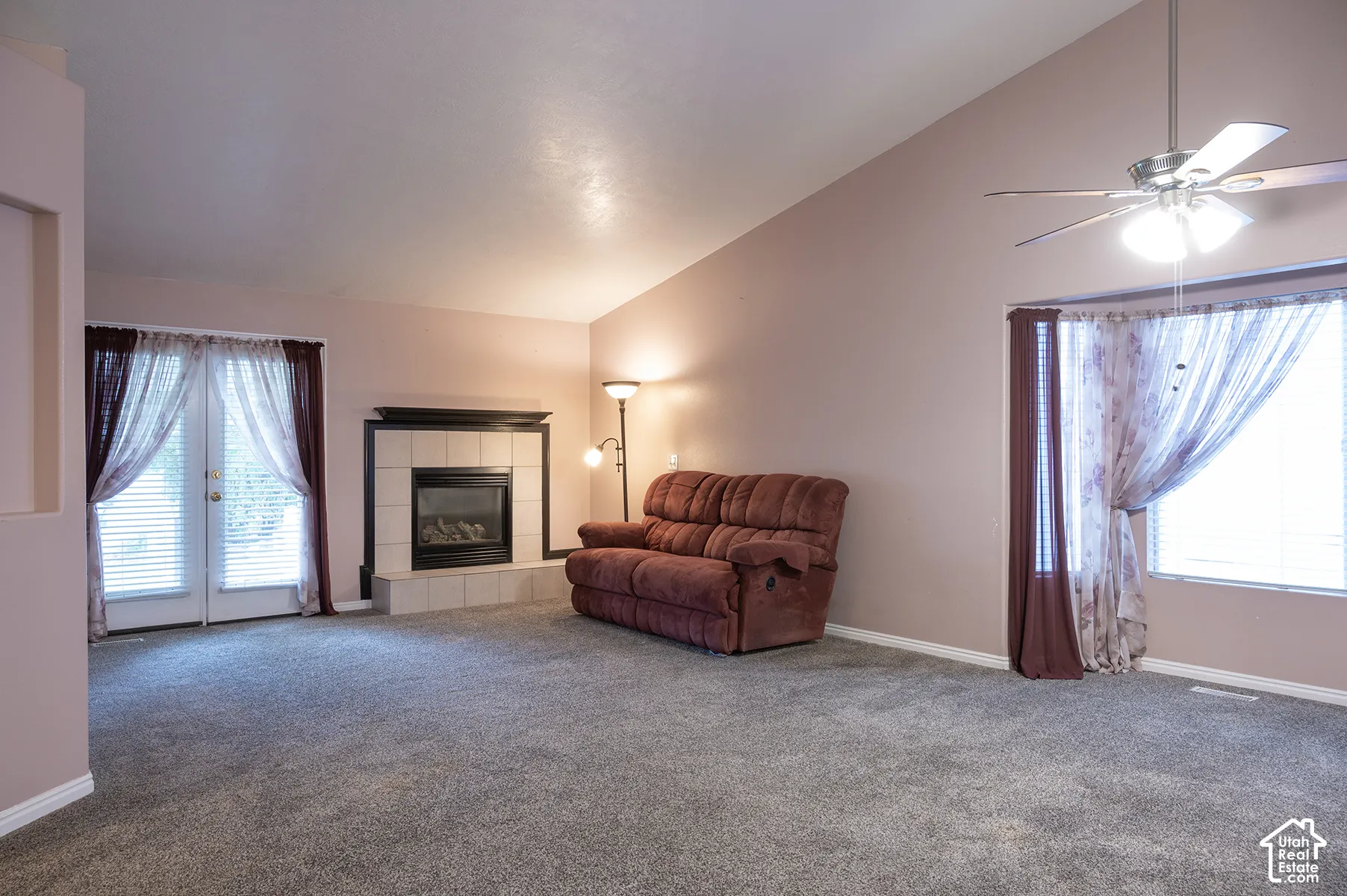 Vaulted ceiling with an integrated overhead lighting fixture, tiled fireplace with a mantel, and double glass-paneled doors