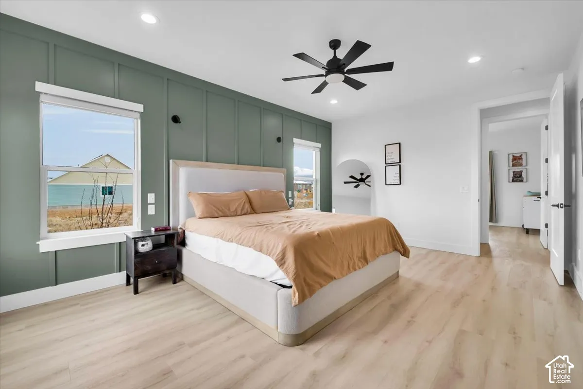 Wood-finish flooring, floor-to-ceiling board and batten accent wall, recessed lighting, matte black ceiling fan, and dual window configuration