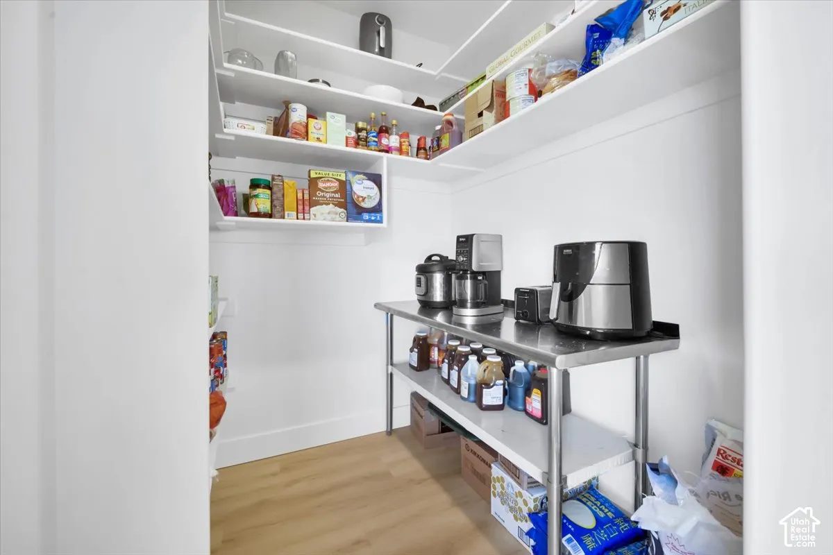 Walk-in pantry featuring white wrap-around shelving and wood-finish flooring