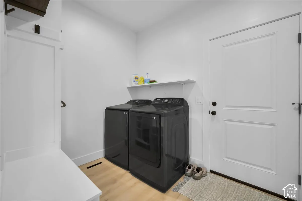 Utility room featuring wood-finish flooring, built-in mudroom cabinetry, a wall-mounted shelving unit, and a solid-core exterior door