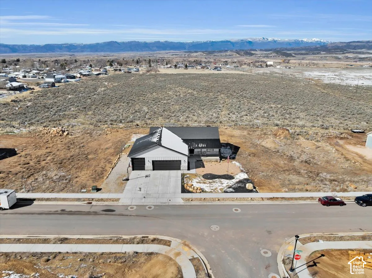 Aerial perspective of a single-story residence featuring a dual-garage configuration, metal roofing, and expansive mountain scenery