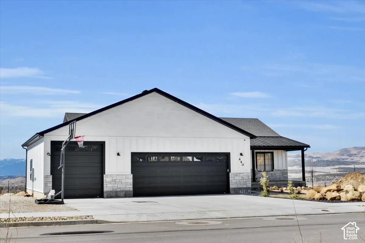Exterior featuring board-and-batten siding, stone masonry accents, a metal roof, and a three-car garage