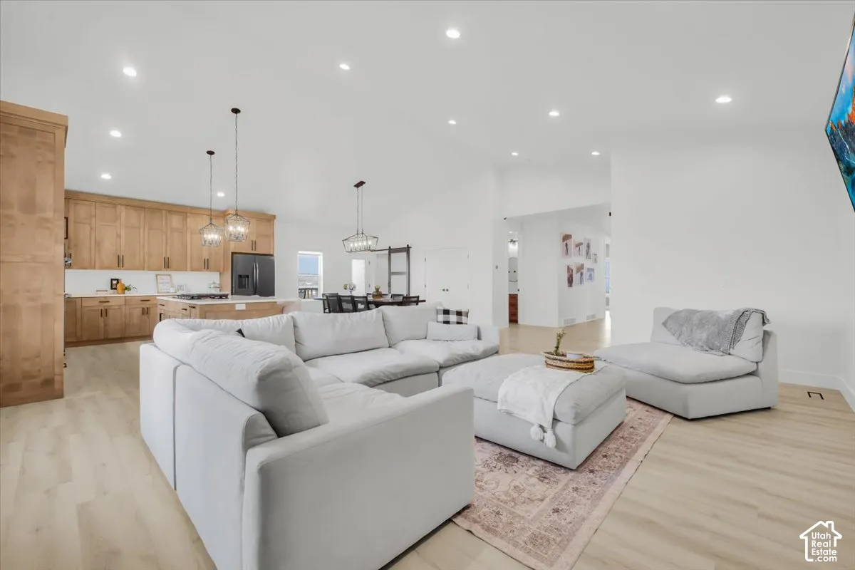 Open-concept space featuring vaulted ceilings, light-tone wood-finish flooring, recessed lighting, and kitchen cabinetry with a natural wood finish