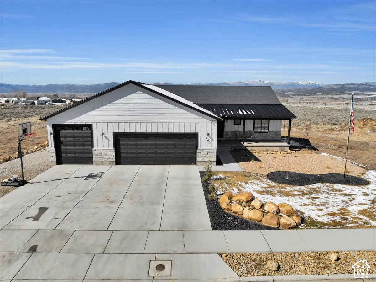 Modern exterior featuring white vertical siding, black metal roofing, stacked stone accents, a multi-car garage, and a mountain backdrop