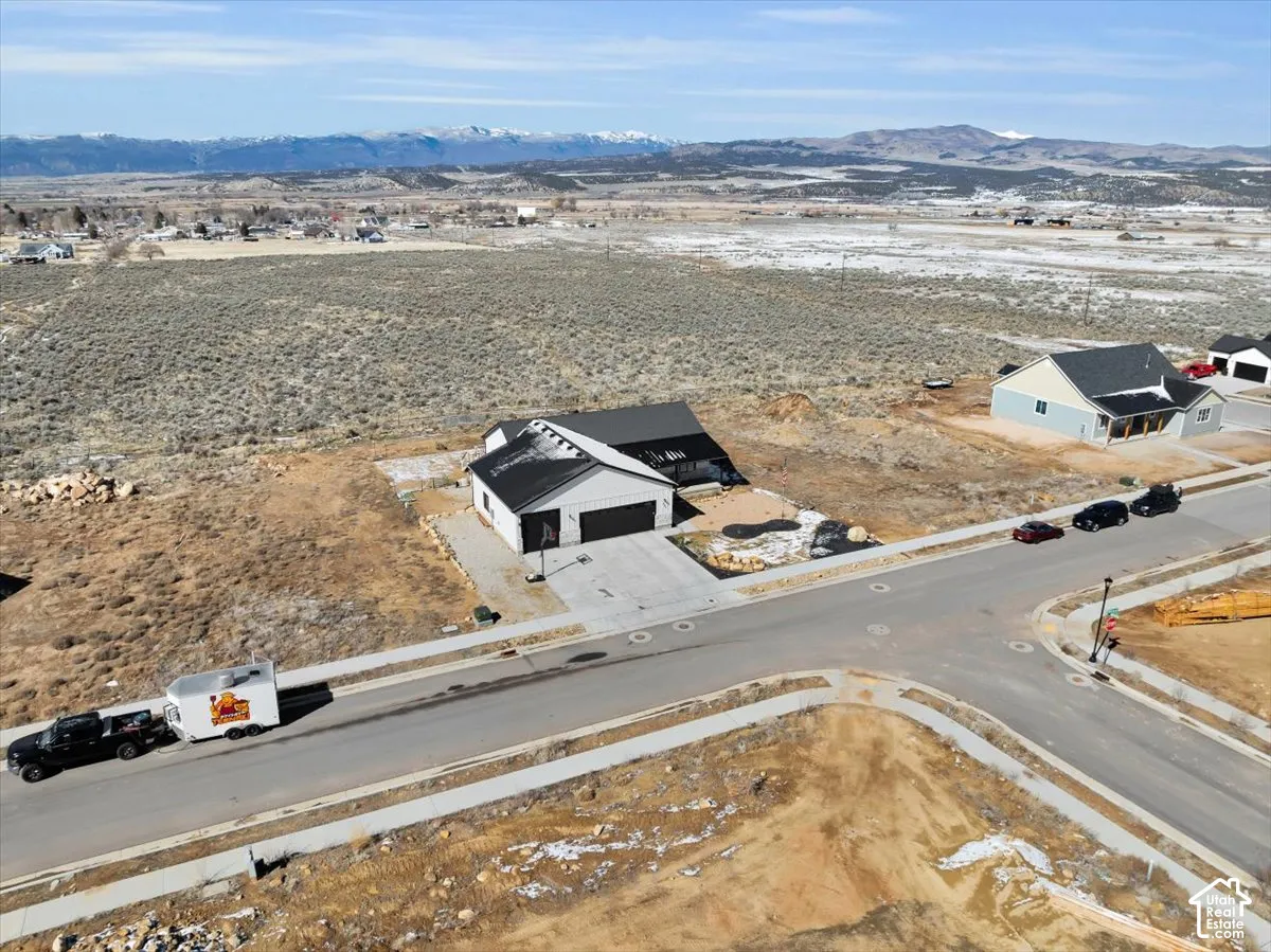 Aerial perspective of a single-story residence featuring a dark-toned gabled roof, concrete driveway, and mountain backdrop